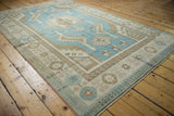 Corner view of distressed Turkish Oushak rug with denim blue field and rose pinwheel motifs.