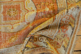 Folded Khotan rug in terracotta, ivory, and saffron, highlighting worn texture and patterns.