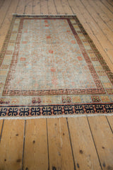 Distressed vintage Khotan rug's navy blue infinity border, terracotta motifs, and white fringe.