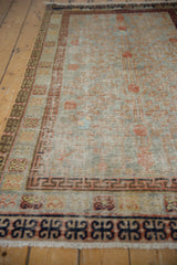 Distressed Khotan rug corner with worn pile, geometric borders, and muted terracotta, slate blue.