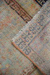 Distressed Khotan rug corner revealing worn pile, muted colors, and hand-knotted foundation.