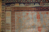 Distressed Khotan rug corner, slate blue field, terracotta vase motifs, and navy geometric borders.