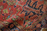 Hand-knotted Heriz rug: brick red ground, navy, blush, celadon, gold floral motifs, aged texture.