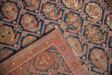Detail of folded antique Afshar rug, repeating indigo, red boteh design, banded border, worn texture.