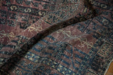 Close-up of vintage Turkmen rug's distressed texture showing aubergine and charcoal motifs.