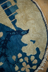 Antique Peking round rug's pictorial blue tree motif on beige ground with tattered fringe.