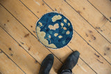 The tattered edge of the antique Peking round rug, featuring indigo and ivory foliage.