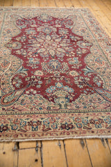 Distressed vintage Sarouk rug corner, featuring wine red field, ivory border, and delicate curvilinear florals.