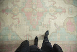 Distressed vintage Oushak carpet with worn pile, geometric patterns in ivory, pink, dusty blue.