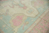Faded ivory, pink, and dusty powder blue serrated motifs on a distressed Oushak carpet.
