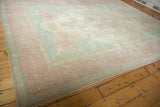 Distressed Oushak rug corner showing pink border with arrow motifs and dusty blue field.