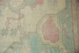 Close-up of distressed Oushak rug's ivory, pink, blue geometric patterns and worn pile.