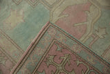 Folded Oushak rug corner revealing distressed pink and blue field motifs, intact selvage.