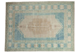 Distressed Oushak rug with elongated medallion, primitive blossoms in faded ivory, beige, and blues.