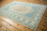 Distressed ivory Oushak medallion with pale blue border and primitive blossoms.