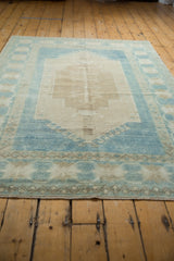 Vintage distressed Oushak rug: faded ivory central field, pale blue geometric border and selvage.