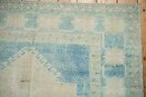 Distressed Oushak rug corner, pale sapphire and sand tones, showing primitive blossoms and intact selvage.