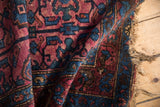 Folded Vintage Lilihan rug with tattered fringe, showcasing rich raspberry and sapphire floral motifs.