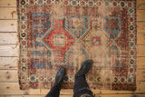 Antique Caucasian rug close-up showing geometric border, tattered edge, and foundation wear.