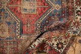 Intricate geometric patterns and exposed foundation of a worn antique Caucasian rug in terracotta and blue.
