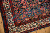 Malayer rug corner displays a blossomed plant ivory border contrasting an indigo Herati field.