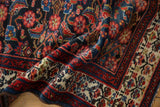 Folded Malayer rug detail: cream main border with blossomed plant motif, indigo Herati field.