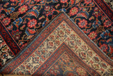Folded corner of a vintage Malayer rug showing hand-knotted foundation and colorful blossomed border.