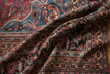 Intricate ruby, sapphire, and beige floral border patterns on the folded vintage Doroksh carpet.