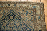 Corner of distressed vintage Malayer rug with fringe and patterned borders in blue, brown.