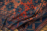 Folded antique Caucasian rug, indigo geometric border, brick red field with repeating gul motifs, storied texture.