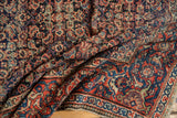 Folded antique Fereghan carpet showing intricate Herati pattern in navy blue and brick red.