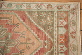 Distressed Oushak runner corner with dusty raspberry, terracotta, and green floral vine border.