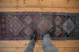 Distressed vintage Oushak runner with worn texture, shown on wood floor with feet.