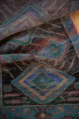 Folded detail of distressed Oushak rug, showing low pile texture and pinkish border edge.