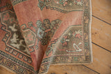 Folded corner of a distressed Oushak rug, showing worn dusty rose pile and geometric motifs.