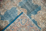 Distressed blue Oushak rug, corner folded revealing fuchsia, ivory, sky blue patterned reverse.