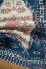 Folded distressed Turkish Oushak rug detail with indigo blue, ivory, blush serrated border.