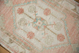 Distressed Oushak rug close-up showing worn pale rose, ivory, and mint green floral motifs.