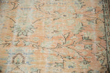 Distressed pile of vintage Turkish Oushak carpet featuring apricot, seafoam green, and ivory vinery.