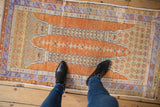 Oushak rug detail: worn orange field, seeded vine pattern, and soft lavender border.