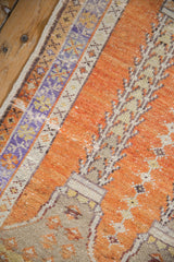 Textured vintage Oushak rug with distressed pale orange field, lavender, and sand floral border motifs.