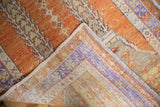 Folded corner of distressed Oushak rug, revealing worn orange, lavender pile and foundation.