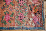 Corner of distressed Oushak rug, showing whimsical floral patterns and blue geometric border.