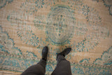 Distressed Oushak carpet with faded beige field, turquoise floral designs, and worn pile.