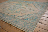 Worn texture of a distressed vintage Oushak carpet with faded beige and turquoise floral motifs.