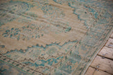 Distressed Oushak carpet's faded turquoise arabesque patterns and worn pile with visible foundation.