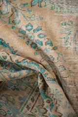 Distressed Oushak rug pile with worn beige tones, exposed foundation, and faded turquoise patterns.