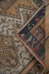 Distressed Oushak rug corner reveals geometric pattern, blue border, and woven selvage.