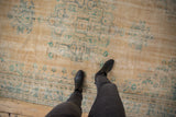 Distressed Oushak carpet with faded turquoise patterns on a beige field, showing wear.