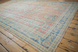 Distressed Oushak carpet corner with faded apricot, blush, and pale denim blue arabesques.